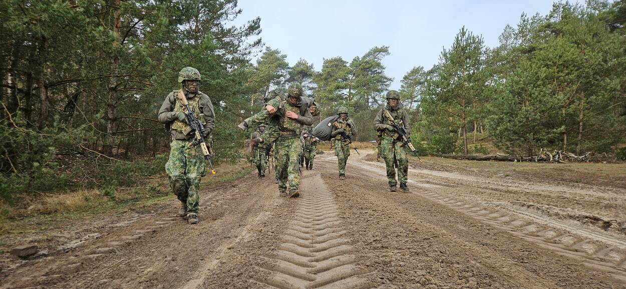 Een groepje reservisten doet verplaatsing te voet, waarbij een van de militairen een gewonden draagt.