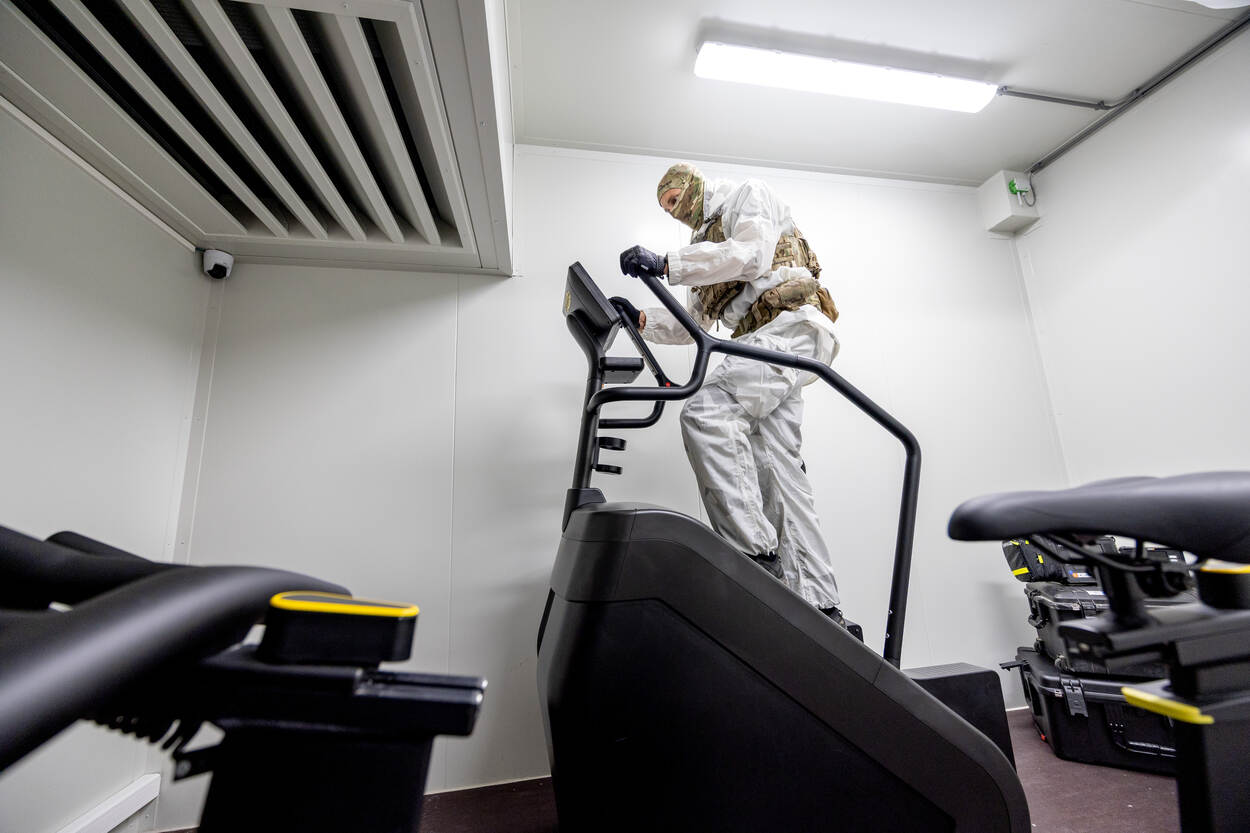 Een militair in wit pak loopt op een fitnessapparaat.