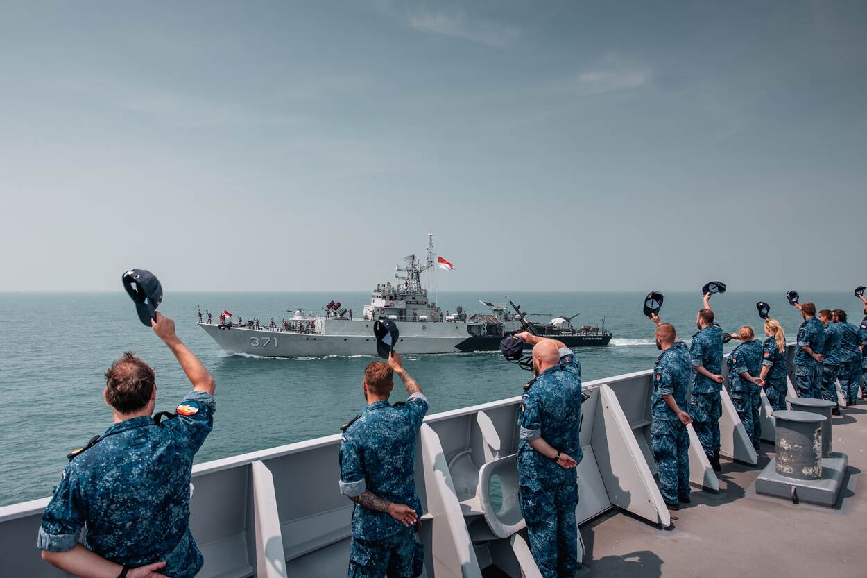 Opvarenden van een marineschip wuiven met hun pet naar een bondgenoot op zee.