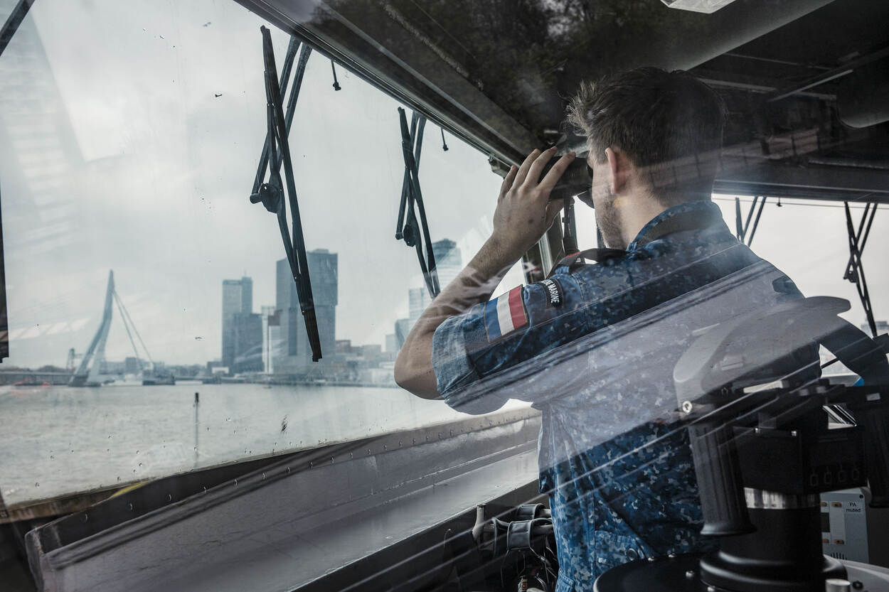 Een collega kijkt door zijn verrekijker naar de Rotterdamse Erasmusbrug.