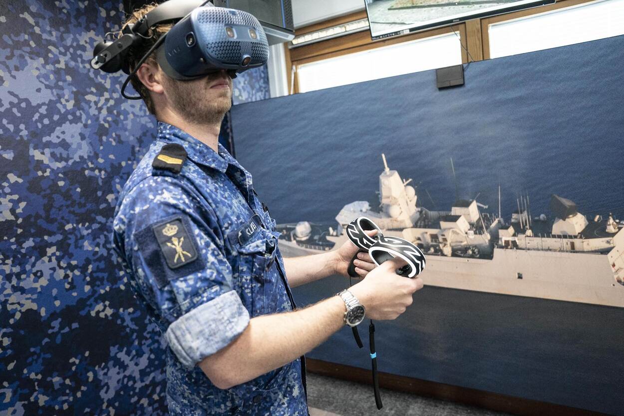 Een marineman in blauw gevechtspak heeft een VR-bril en controllers in zijn handen.