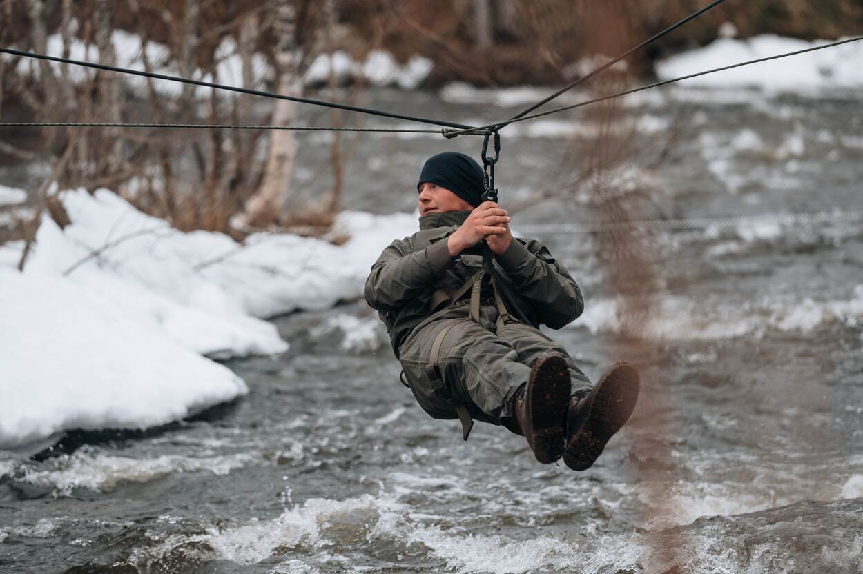 Een marinier hangt aan een touw boven een beek.