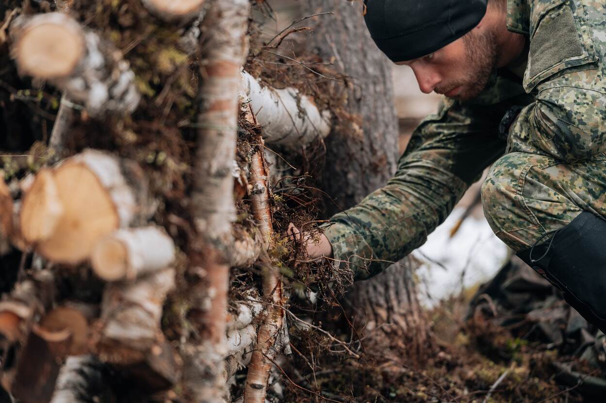 Een marinier bouwt aan een hun van boomstronken, takken en mos.