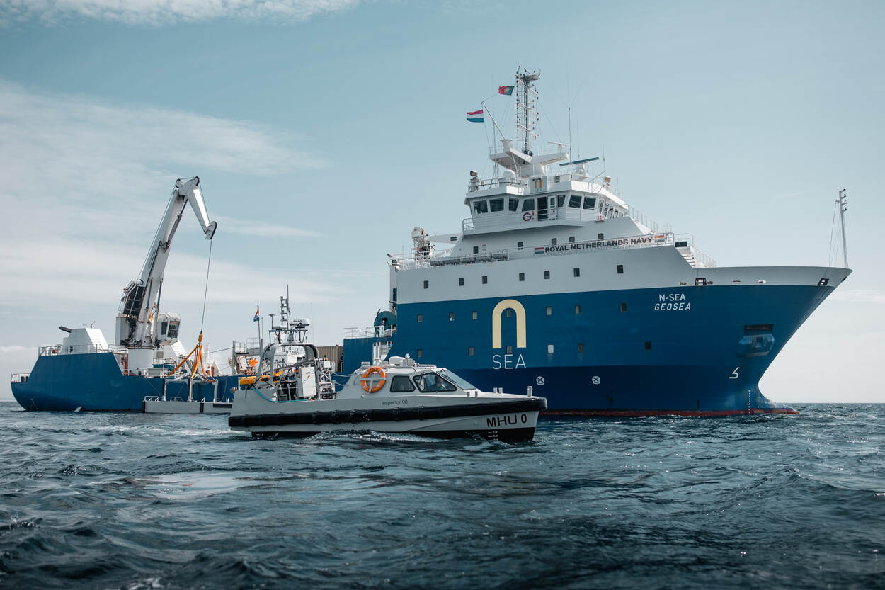 Een mijnenbestrijdingsvaartuig wordt op zee geflankeerd door een kleiner scheepje.
