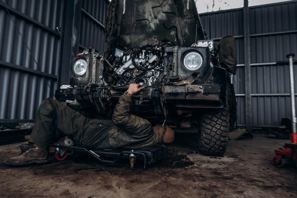 Een militair van de herstelcompagnie ligt op een hondje onder een voertuig. Hij sleutelt aan de CDI.