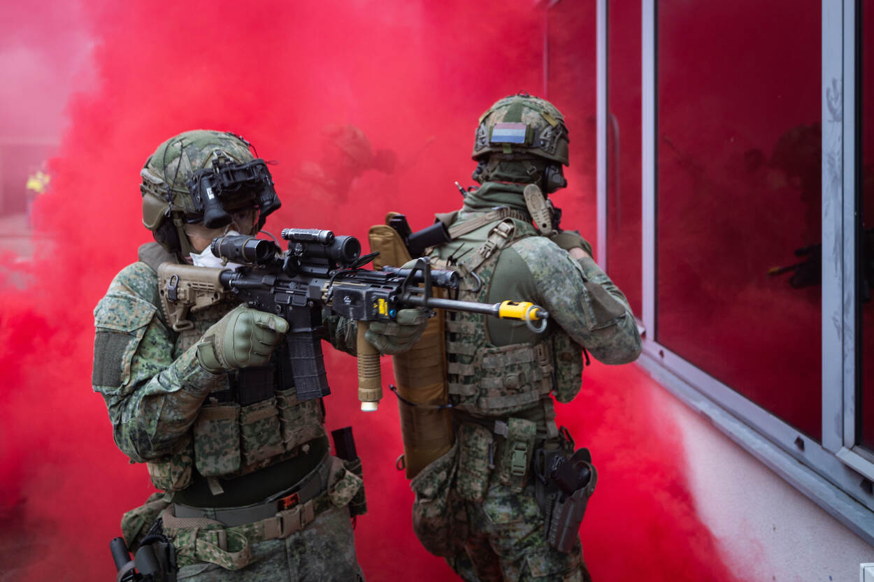 Militairen staan in rode rook, met geweren in de aanslag scannen ze de omgeving.