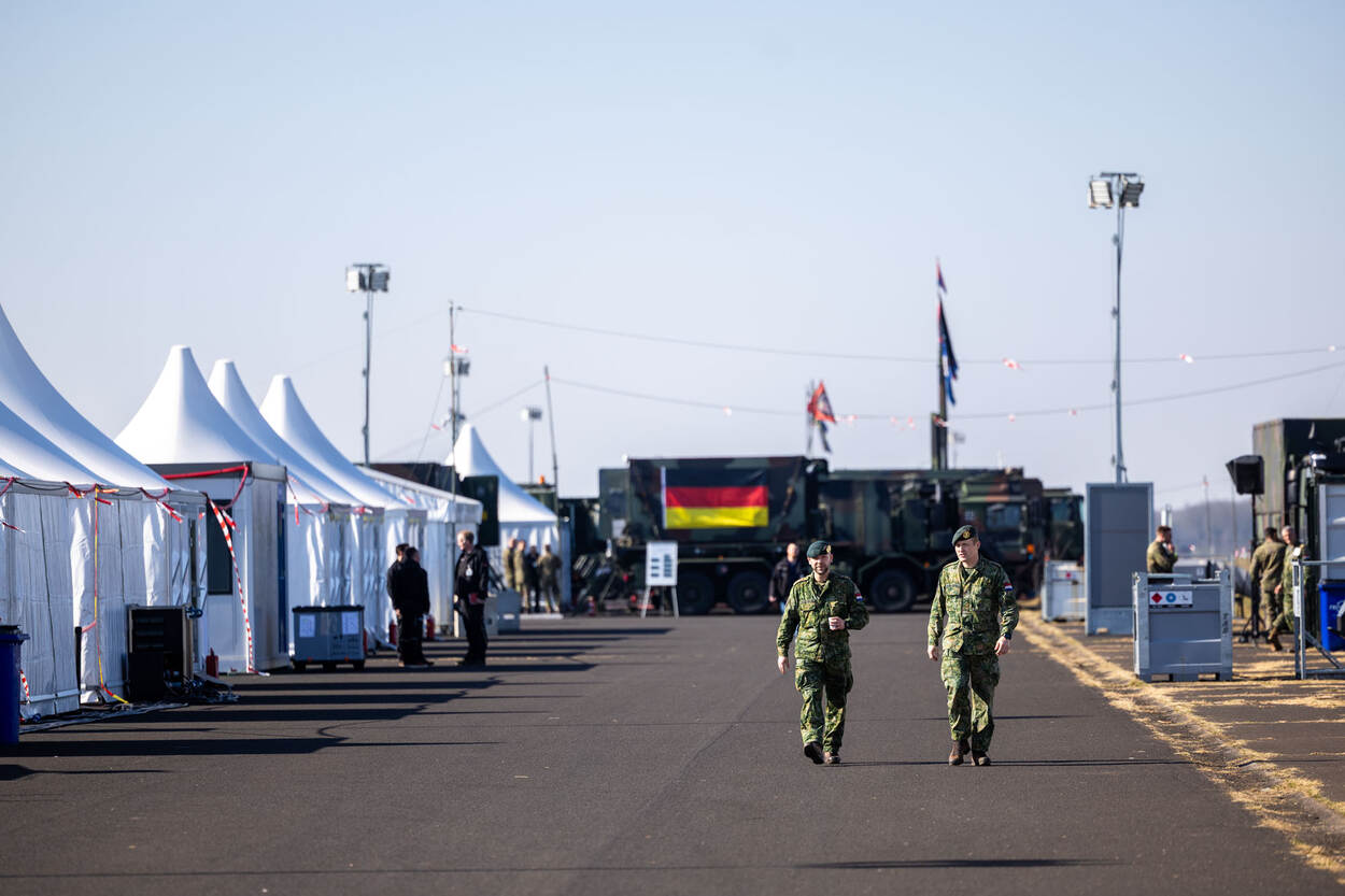 Over het oefenterrein lopen temidden van witte tenten 2 landmachtmilitairen.