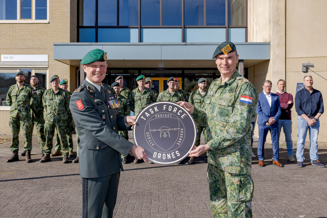 Luitenant-generaal Jan Swillens houdt, samen met brigadegeneraal Joland Dubbeldam een plakkaat in de handen, waarop ‘task force drones’ staat. Achter hen staan militaire en burgercollega’s opgesteld.