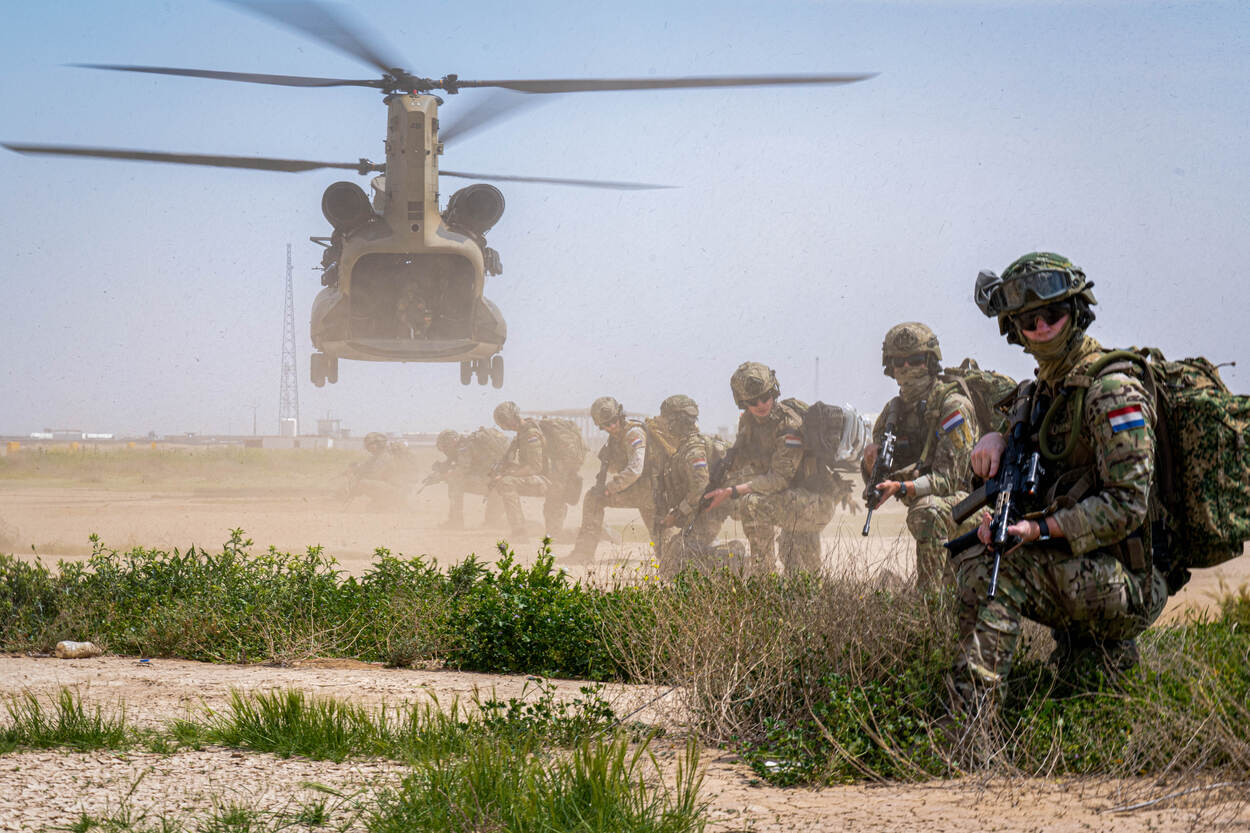 Nederlandse luchtmobielers zijn gepositioneerd op oefenterrein Besmaya in Irak terwijl een Chinook-helikopter opstijgt.