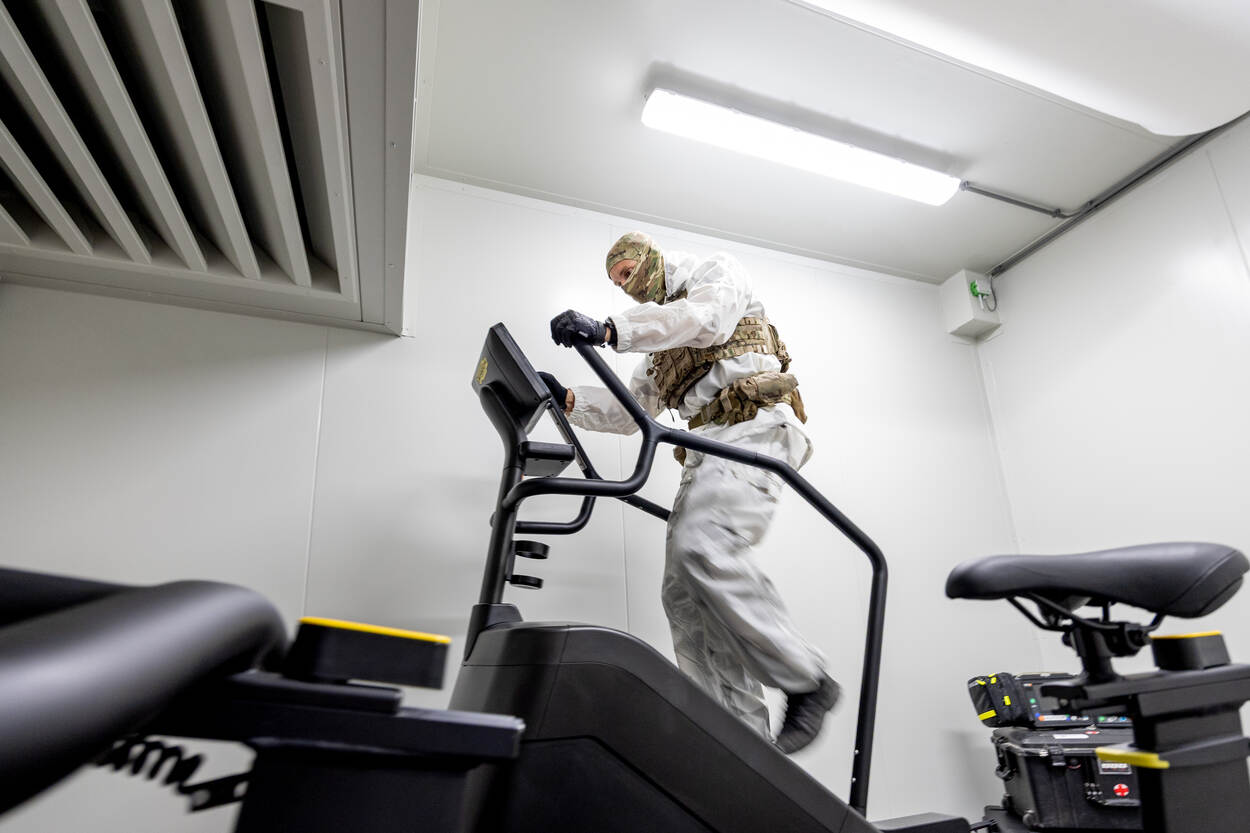 Een militair in wit pak loopt op een fitnessapparaat.
