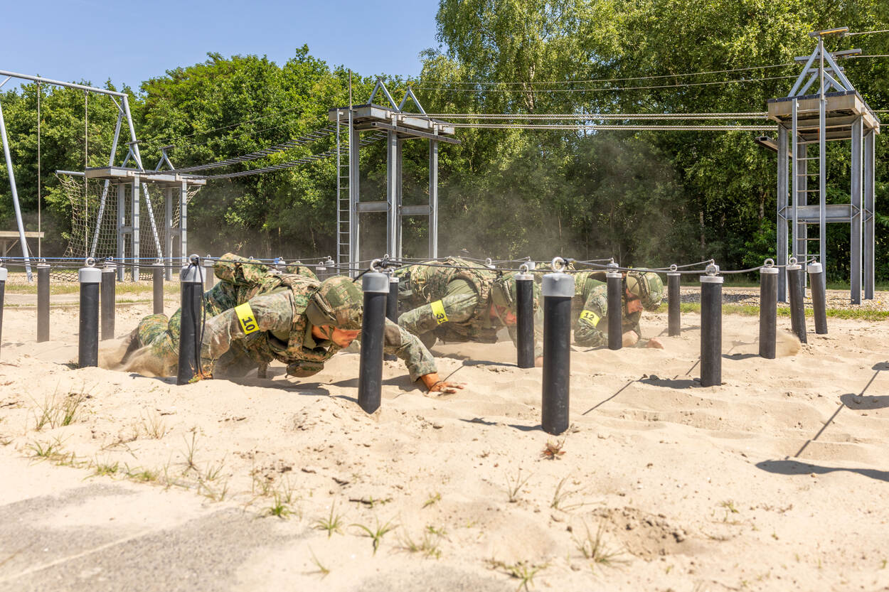 3 militairen kruipen onder draden door het zand.