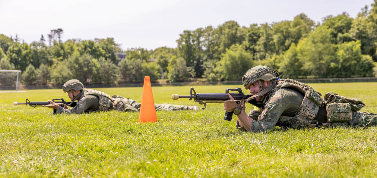 Militairen liggen in het veld en richten hun wapen aan.