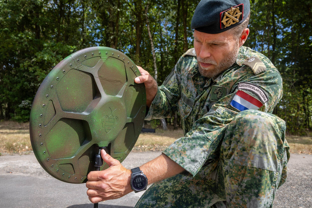 Een militair bevestigt een groen gespoten akoestische sensor op een driepoot.
