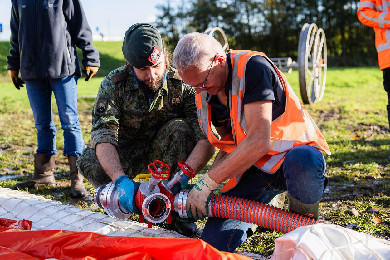 2 mannen leggen een leiding aan van wie 1 in militair tenue.