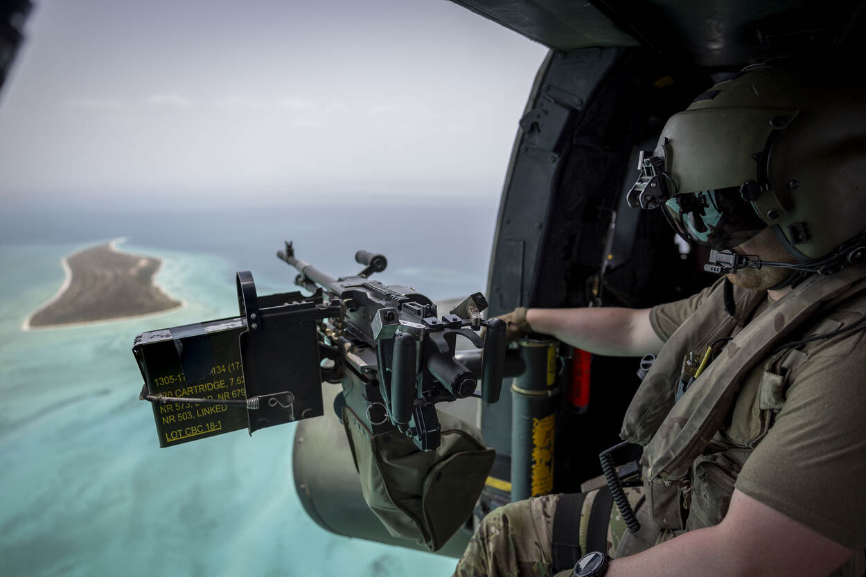 Een boordschutter kijkt door de open deur van de heli naar een eiland in zee.