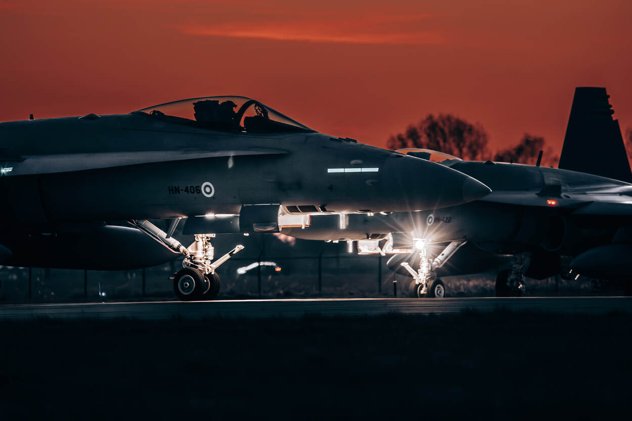 Close up van de voorkant van een Finse F/A-18 met op de achtergrond nog een exemplaar tegen een rode avondlucht als achtergrond.