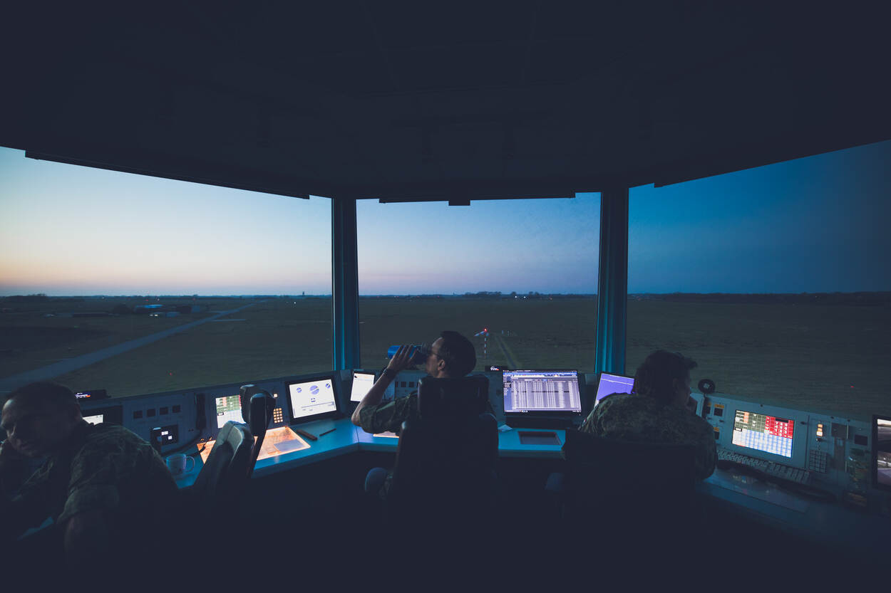 Schemering gezien vanuit de verkeerstoren met op de voorgrond drie luchtverkeersleiders.