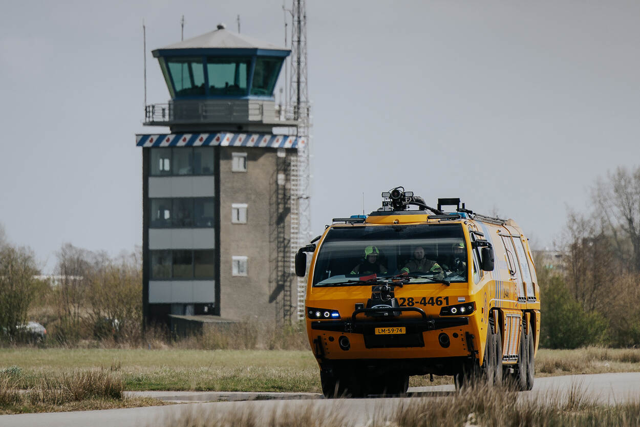 Een E-One crashtender rijdt naar de startbaan. Op de achtergrond de verkeerstoren.