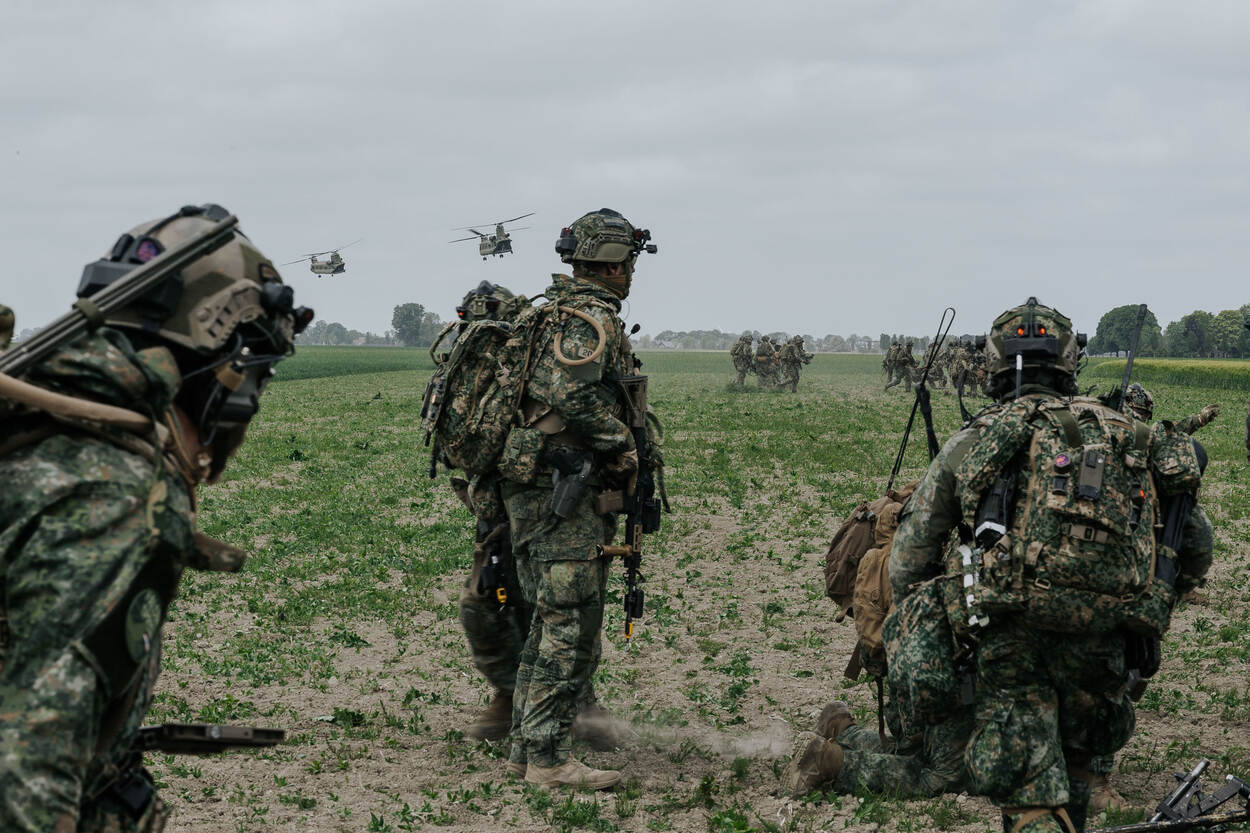 Militairen in het veld met op de achtergrond twee wegvliegende Chinooks.