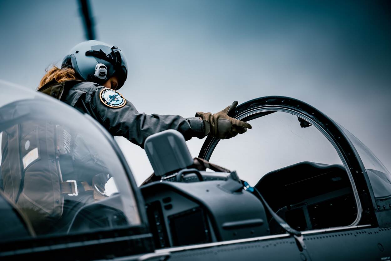 Een vlieger met helm op in de cockpit van een lesvliegtuig.