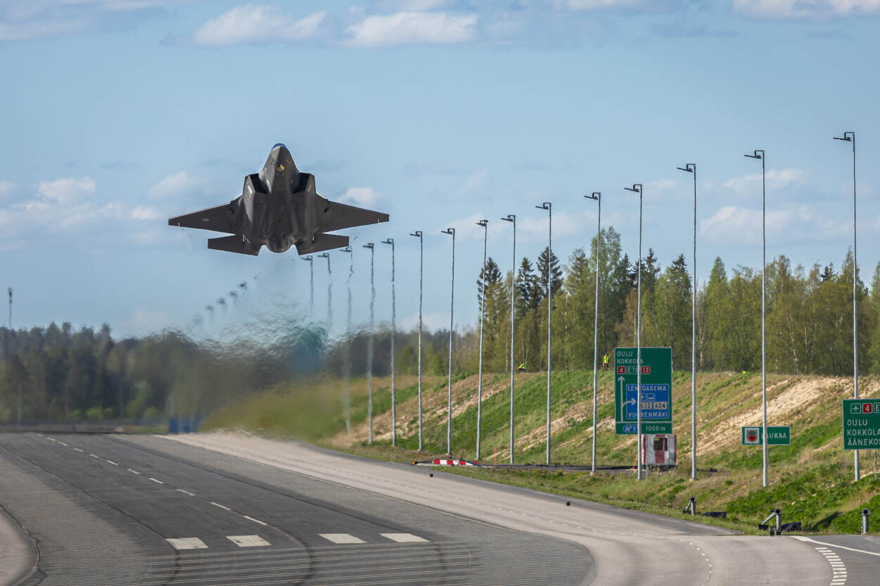 Een F-35 trekt op vanaf de snelweg net voor een bocht, aan de kant staan lantaarnpalen.