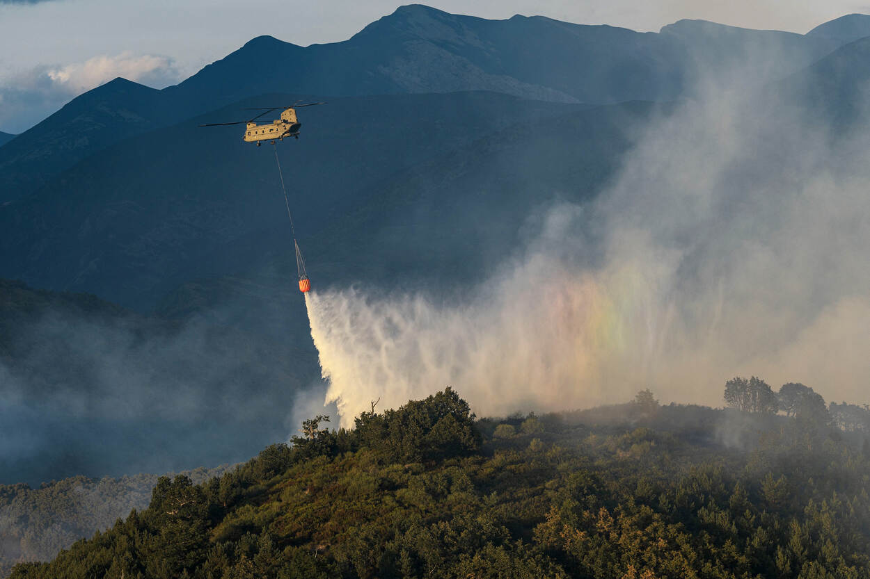 Een Chinook, met daaronder een Bambi Bucket, gooit water over een bosbrand.