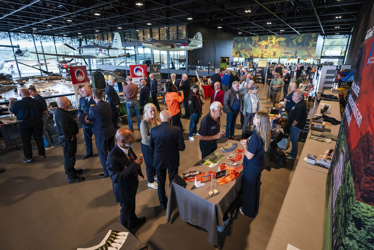 Bezoekers praten met elkaar en kijken bij uitgestalde waar op tafels.