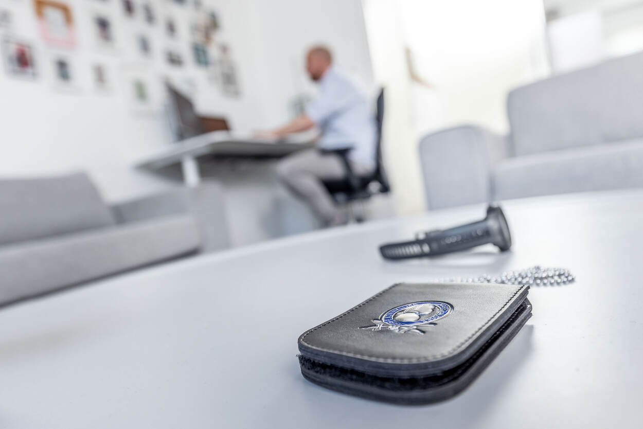 Foto van een collega die bij het cluster Integriteit werkt. Op de voorgrond een badge van de Marechaussee.