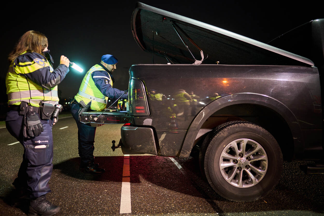 Politieagent en Marechaussee controleren achterbak van een pick-up truck.