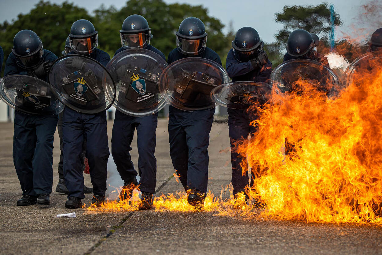 Mobiele Eenheid van de Marechaussee lopen met helm en schild door een vuur.