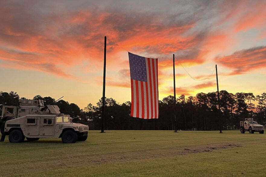 3 militaire voertuigen op een grasveld met in het midden de Amerikaanse vlag