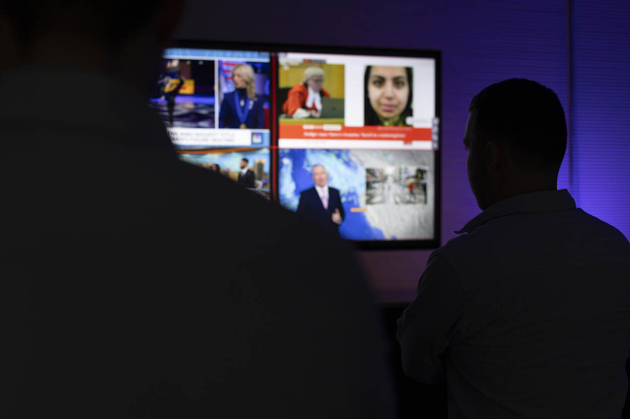 2 slecht zichtbare personen volgen in het donker het nieuws op een groot scherm.