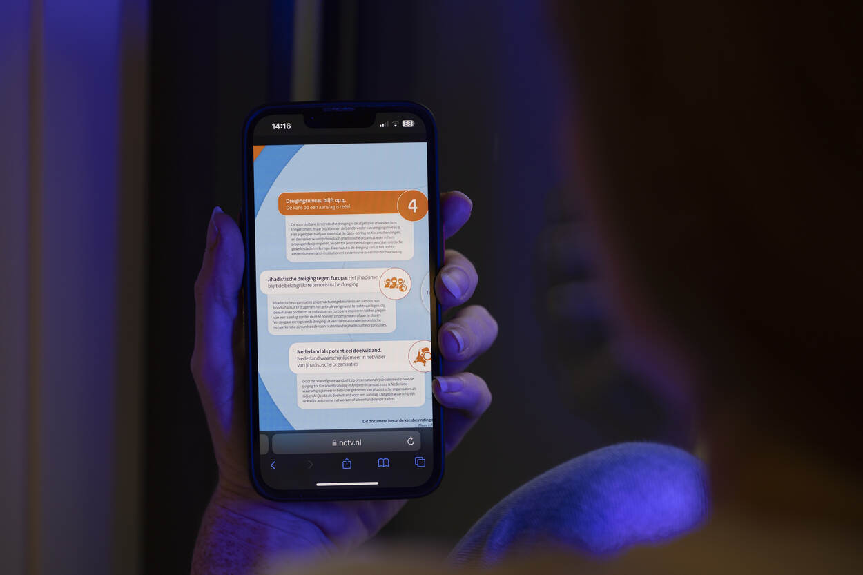 Een persoon bekijkt via mobiele telefoon in zijn hand een pagina van het NCTV.