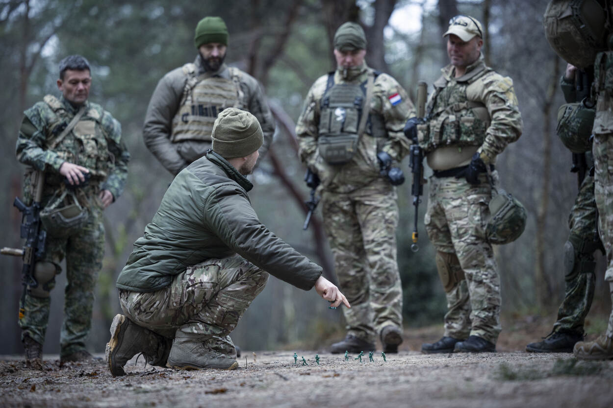 Een instructeur van het IMPT legt wat uit in het bos aan cursisten.