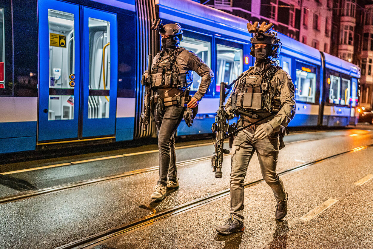 Twee medewerkers van de Dienst Speciale Interventies lopen zwaarbewapend naast elkaar. Daarachter een tram.