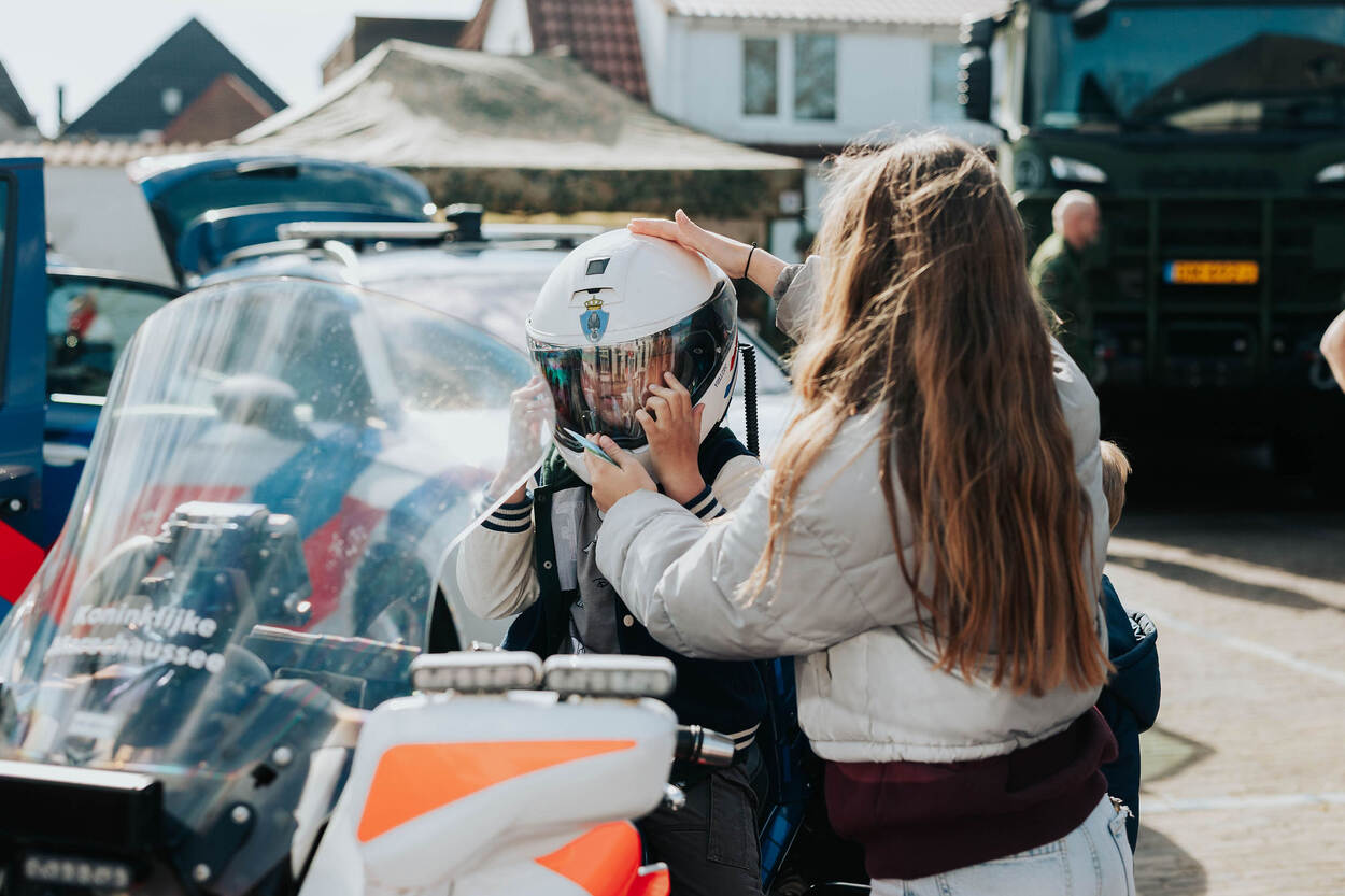 Een jong kind zit op een Marechaussee-motor en krijgt een helm opgezet.