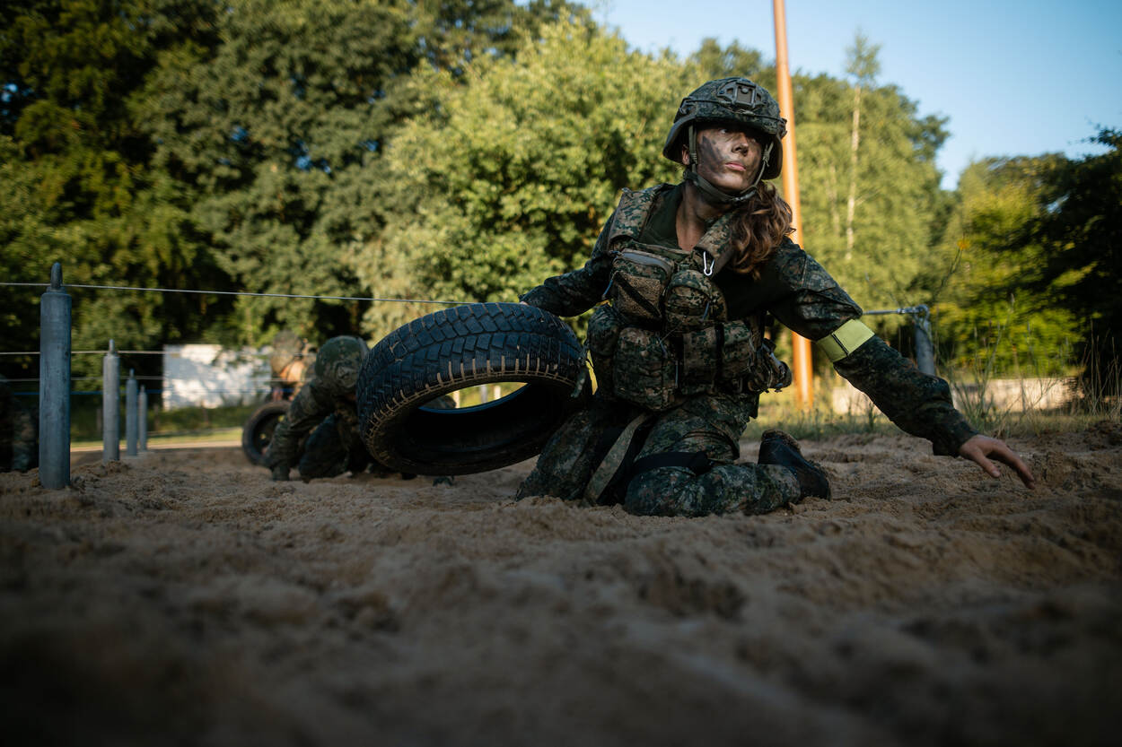 Een marechaussee in opleiding sleept een band voort over de zandvlakte.