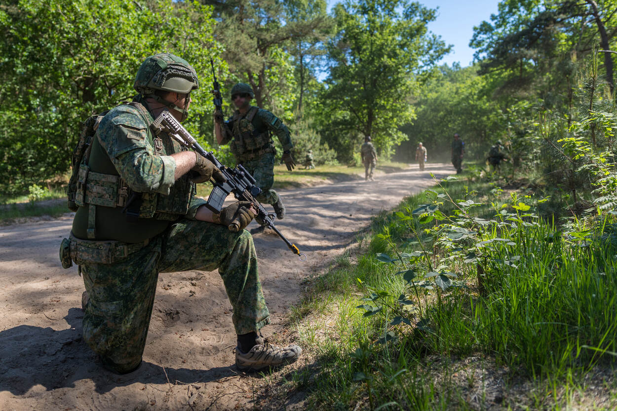 Een groene marechaussee gehurkt op de Ermelosche Heide, achter hem lopen collega’s.