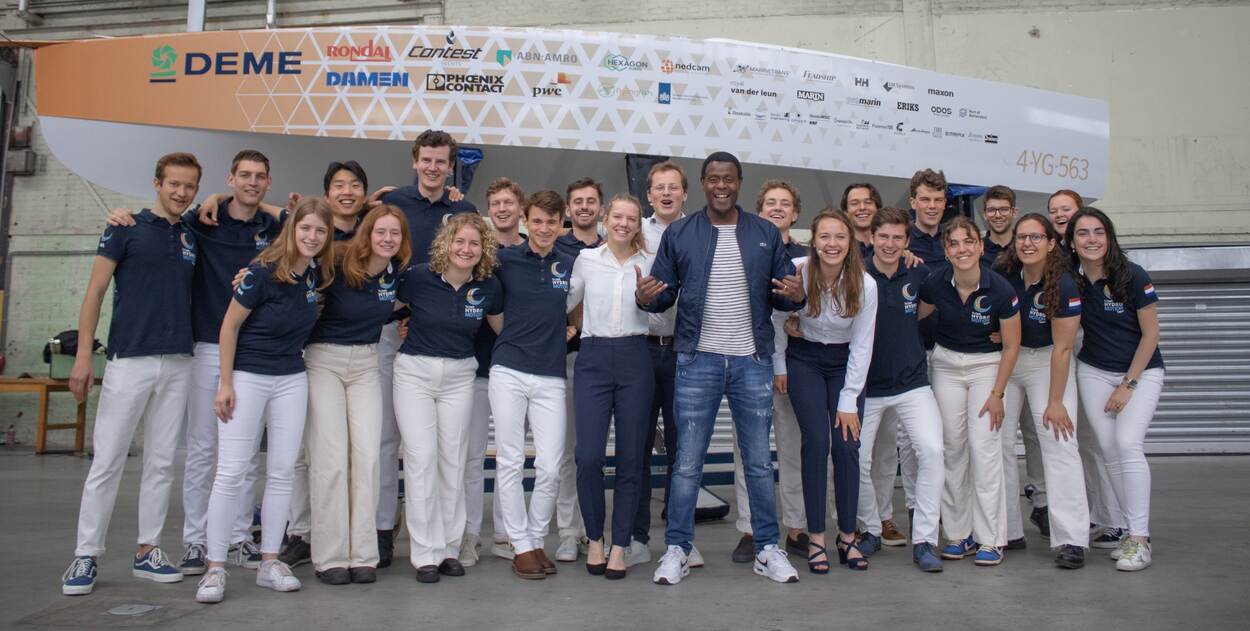 Studenten van de TU Delft poseren met John Williams voor hun waterstofboot.