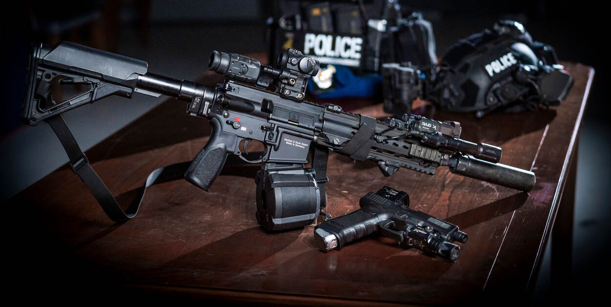 HK 416 met daarvoor een Glock 17 en daarachter helm en scherfvest.