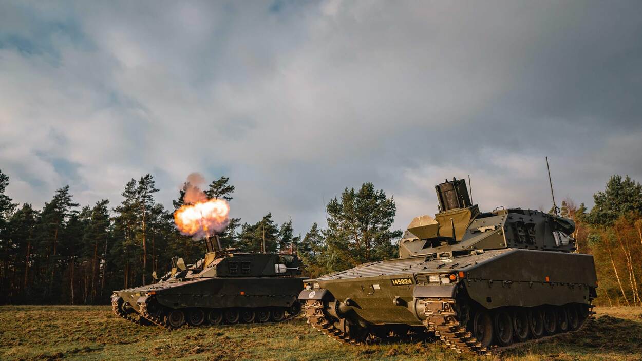 Twee Zweedse Granatkastarpansarbandvagn 90 bij een bosrand waarvan er een vuurt.