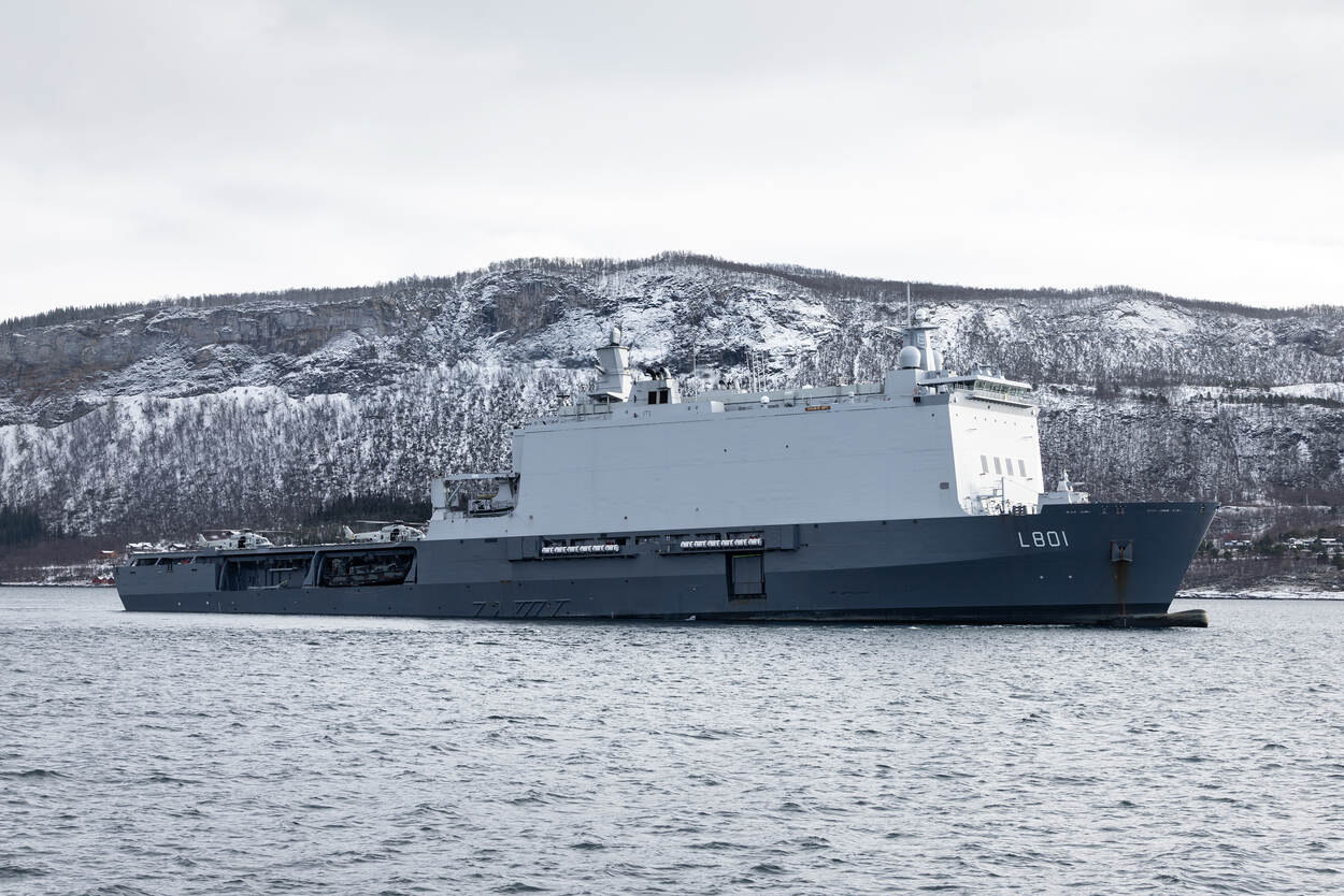 Marineschip met twee helikopters op achterdek ligt langs de kust.