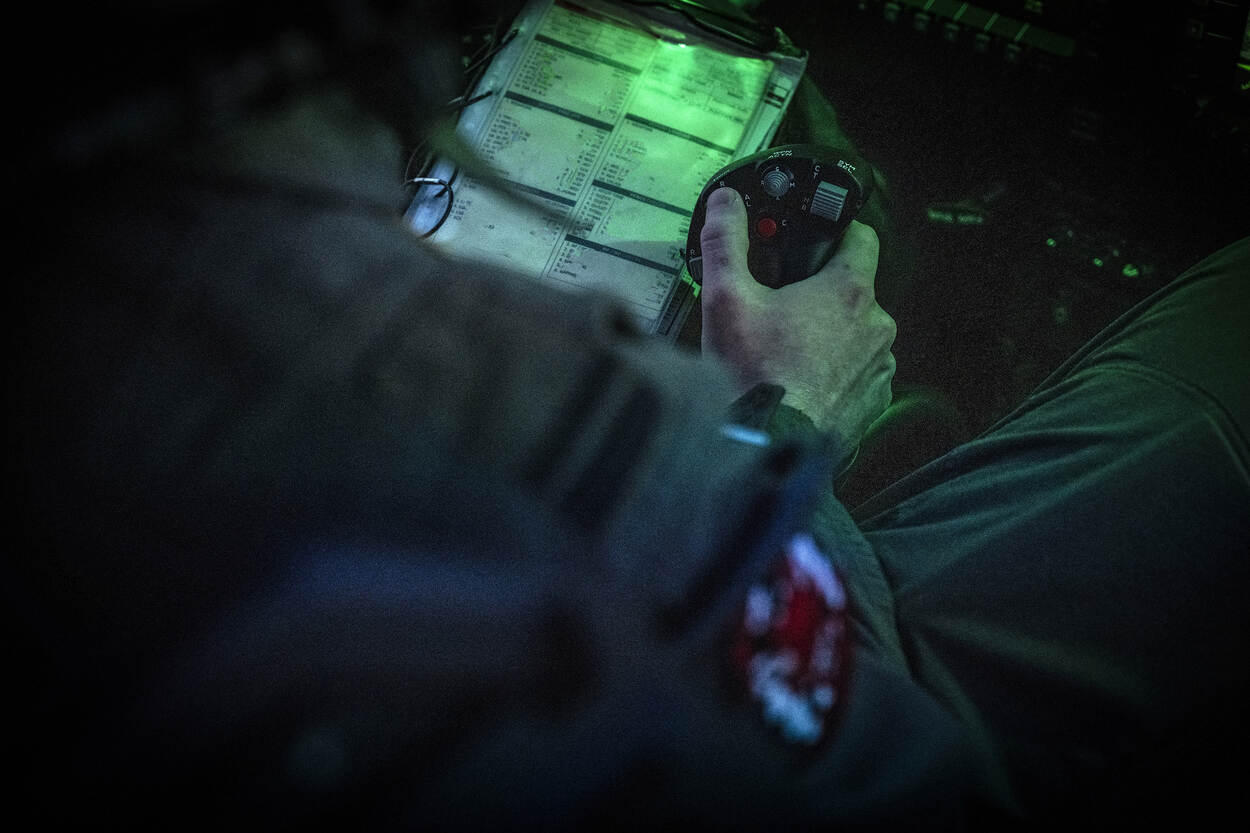 Hand van vlieger houdt een stuurknuppel vast. Op het linkerbeen ligt een clipboard met informatie.