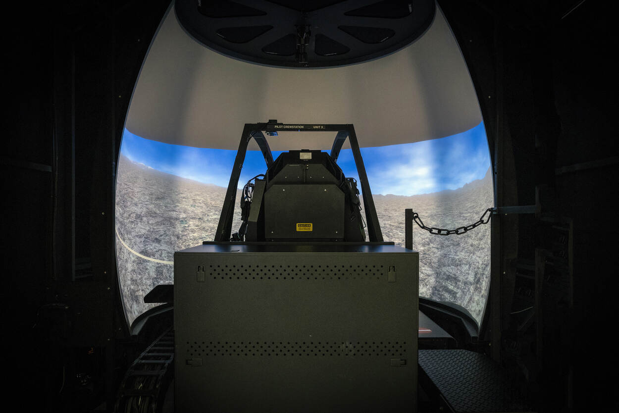 Stoel van helikopterpiloot staat in simulator voor een groot scherm met daarop een virtueel landschap.