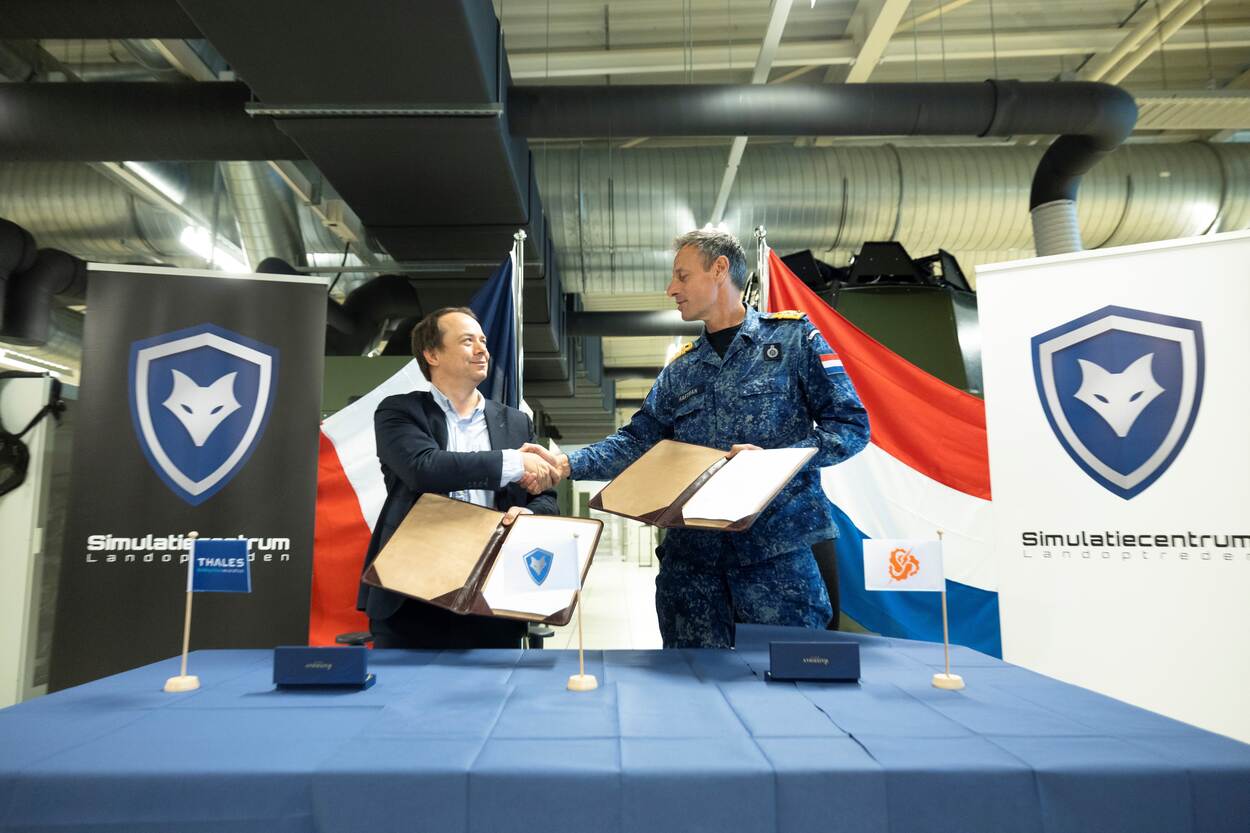 staan beide heren handenschuddend achter een bureau.