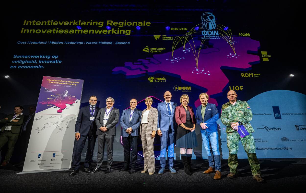 De ondertekenaars staan op een podium met de handtekeningen