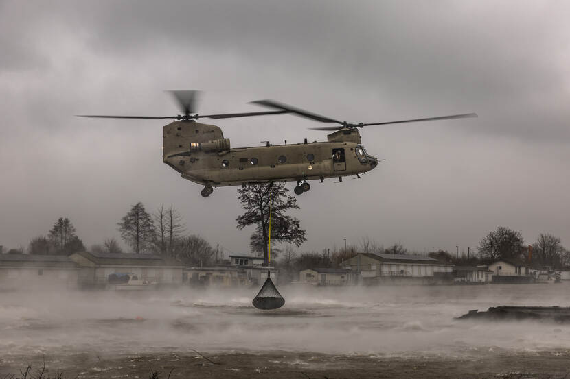 Een Chinook dropt een net vol stenen in het water.