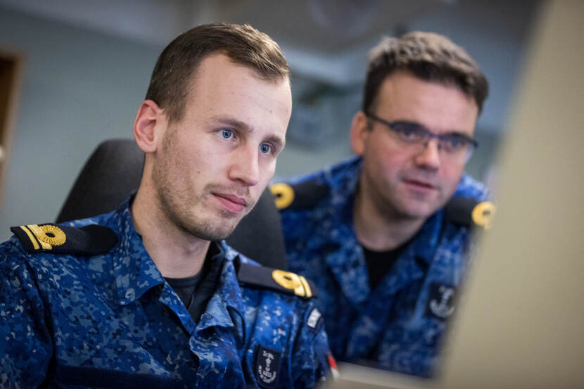 Systeemofficier Leon kijkt naar een scherm, terwijl een collega over zijn schouder meekijkt.