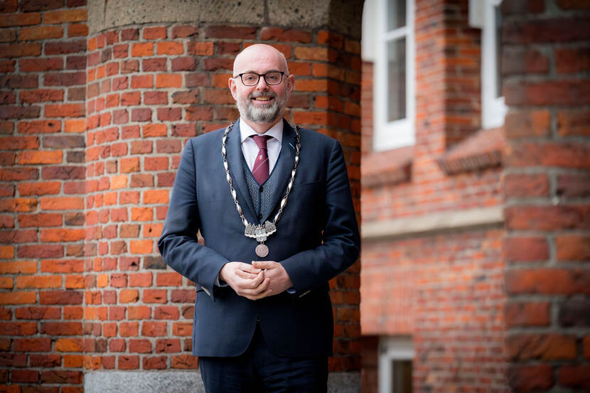Liggende foto van burgemeester Martijn Vroom met z’n ambtsketen om, voor het gemeentehuis van Leidschendam-Voorburg.