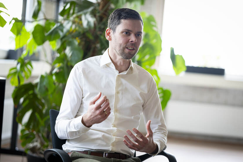 Auteur Jori Kalkman met een wit overhemd aan tafel met zijn armen gebarend.
